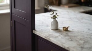 "white marble countertop with grey veining on aubergine kitchen cabinet"